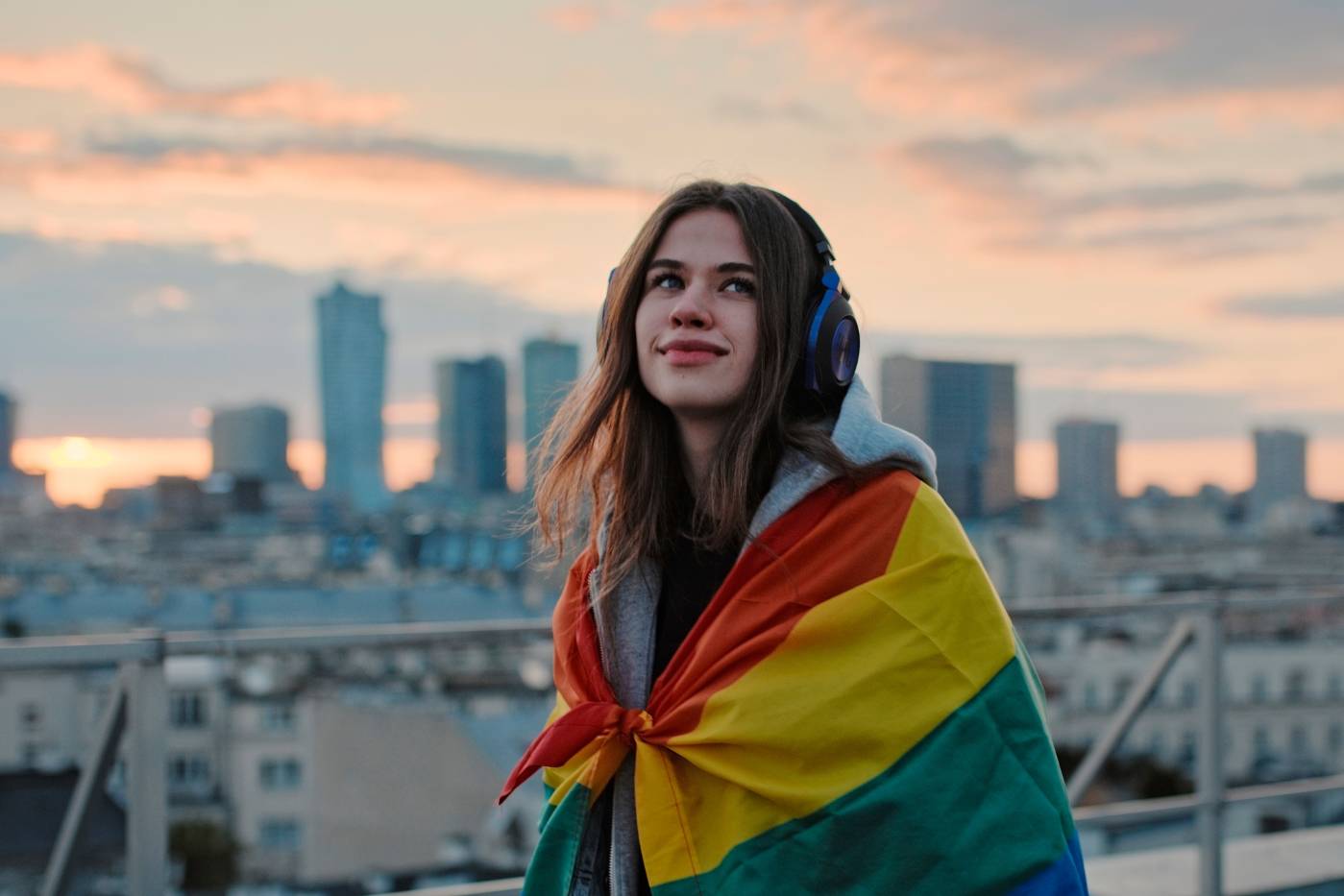 Une femme regarde l'horizon. Elle est couverte par un drapeau au couleur LGBT