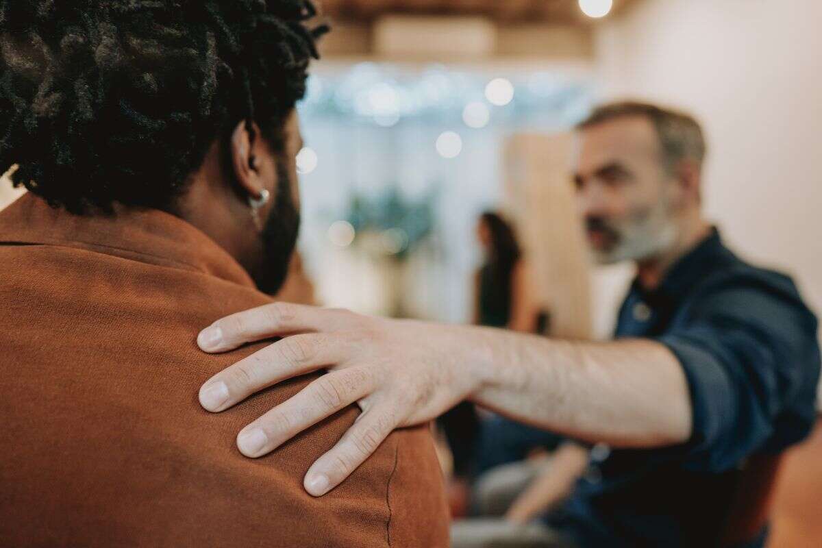 Deux personnes échangent dans un espace intérieur, l’une posant une main rassurante sur l’épaule de l’autre.