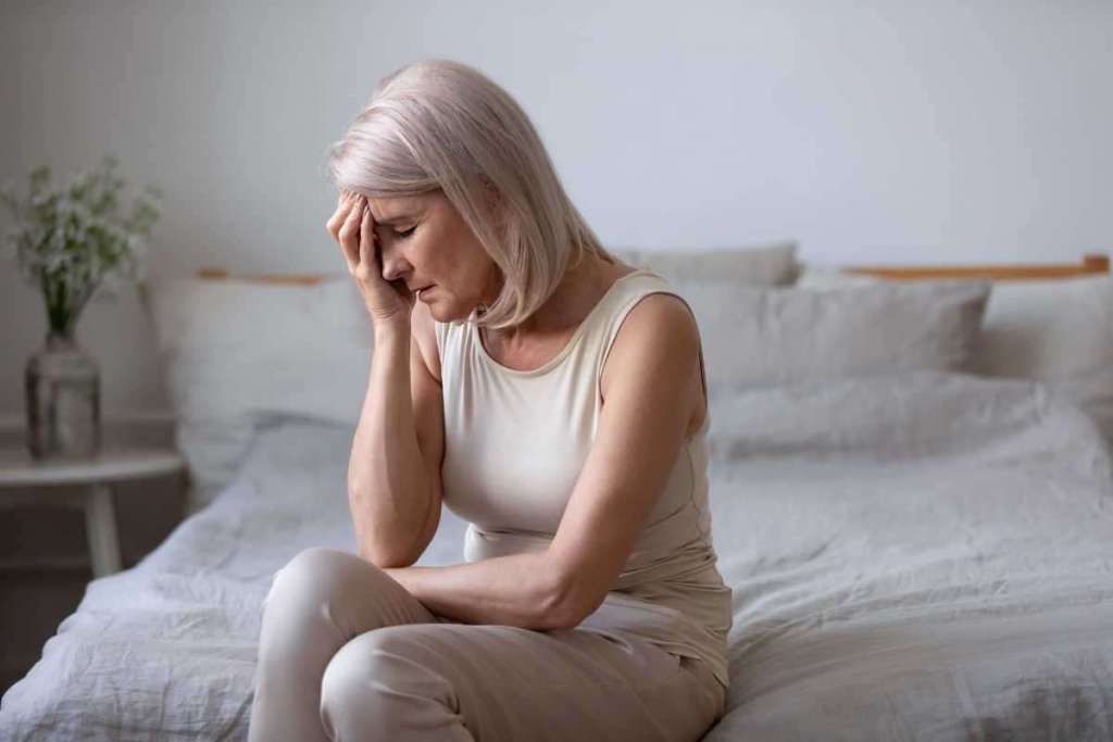 Une femme en pleine ménopause de tient la tête sur son lit
