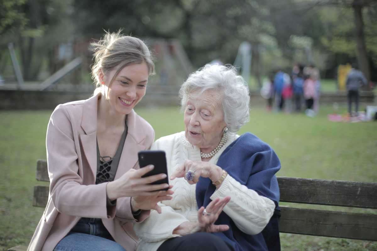 deux dames discutent sur un banc. une dame jeune montre son téléphone portable a une femme âgée